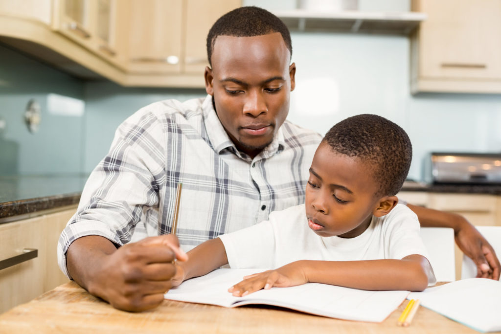 Adult helping young boy with effective studying in kitchen